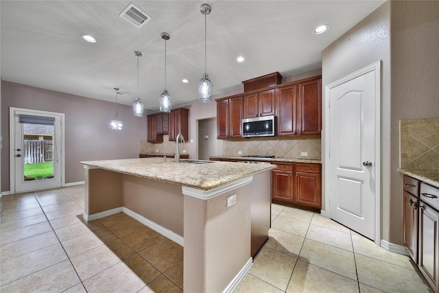 12119 Bayou Junction Rd, Cypress, TX 77433 - kitchen with stainless steel microwave, a sink, backsplash, an island with sink, and light tile patterned floors