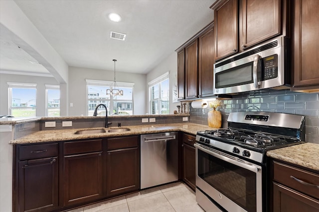 10744 S Lake Mist Ln, Willis, TX 77318 - kitchen with stainless steel appliances, a sink, light stone countertops, dark brown cabinetry, and a peninsula
