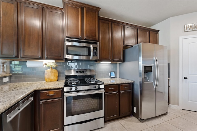 10744 S Lake Mist Ln, Willis, TX 77318 - kitchen featuring appliances with stainless steel finishes, decorative backsplash, light tile patterned floors, light stone counters, and dark brown cabinets