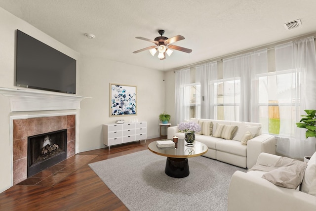 6010 Twin Crk, Missouri City, TX 77459 - living room featuring ceiling fan, dark wood-style flooring, a tiled fireplace, and a textured ceiling