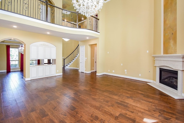 5450 Pudman River Ln, Sugar Land, TX 77479 - unfurnished living room with a glass covered fireplace, baseboards, dark wood-style floors, a towering ceiling, and a chandelier