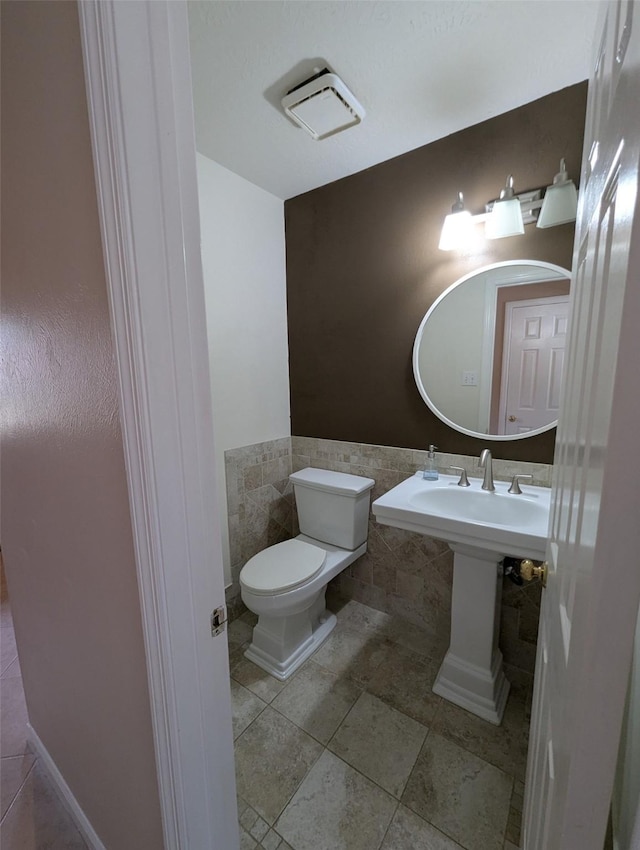 half bath with tile walls, toilet, a wainscoted wall, and tile patterned floors
