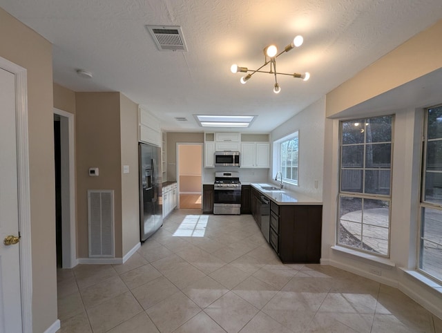 kitchen with appliances with stainless steel finishes, a sink, white cabinetry, light tile patterned flooring, and a textured ceiling