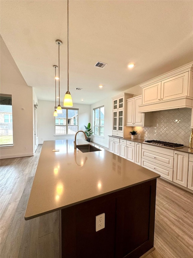 1215 Tallow Park Ln, Pinehurst, TX 77362 - kitchen featuring stainless steel gas cooktop, light wood finished floors, tasteful backsplash, a center island with sink, and hanging light fixtures