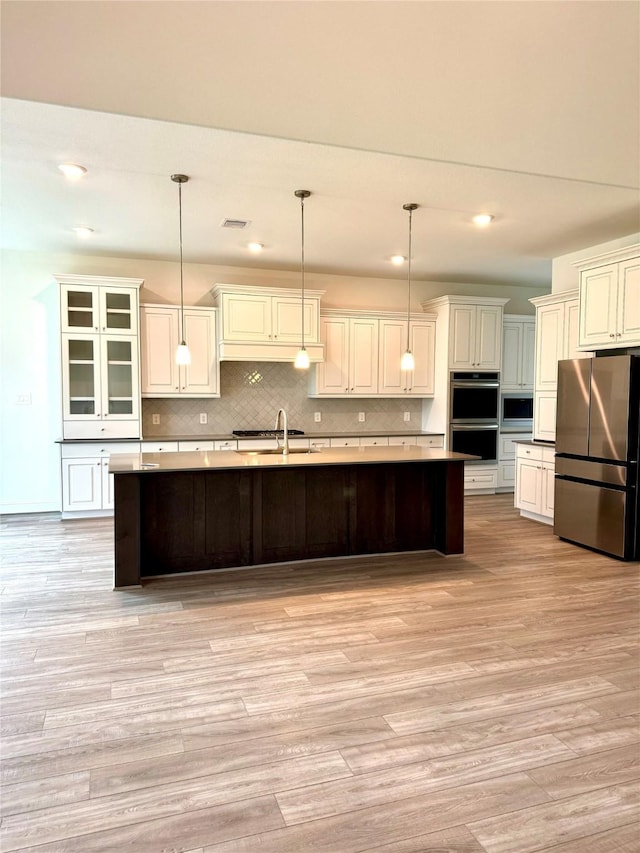 1215 Tallow Park Ln, Pinehurst, TX 77362 - kitchen featuring stainless steel appliances, a sink, light wood-style flooring, a spacious island, and tasteful backsplash