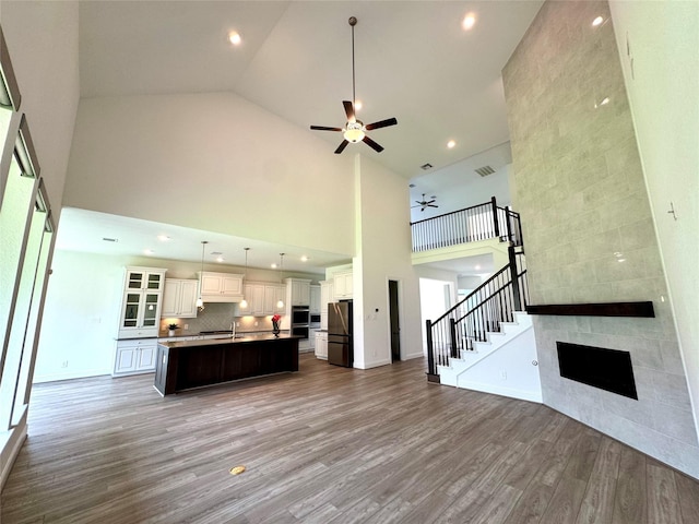 1215 Tallow Park Ln, Pinehurst, TX 77362 - unfurnished living room with a ceiling fan, high vaulted ceiling, light wood-type flooring, a tile fireplace, and stairs