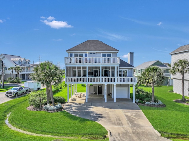 coastal home with an attached garage, driveway, a balcony, a front yard, and roof with shingles