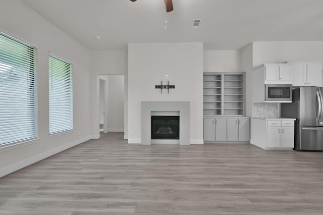 10066 Preserve Way, Conroe, TX 77385 - unfurnished living room with a ceiling fan, light wood-type flooring, a glass covered fireplace, and baseboards