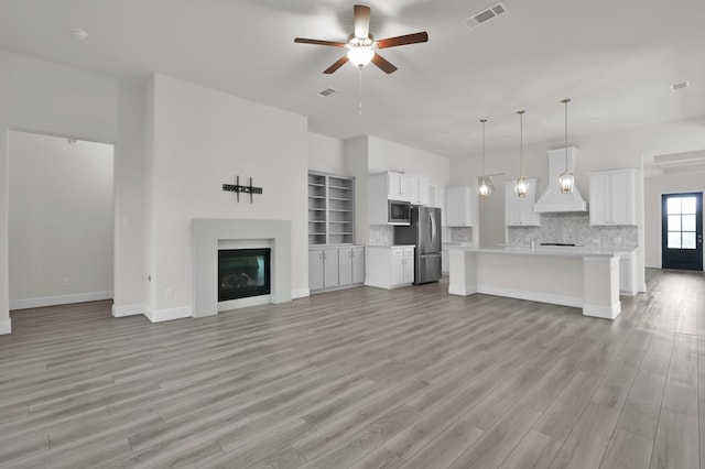 10066 Preserve Way, Conroe, TX 77385 - unfurnished living room featuring a ceiling fan, light wood-style flooring, a glass covered fireplace, baseboards, and a sink