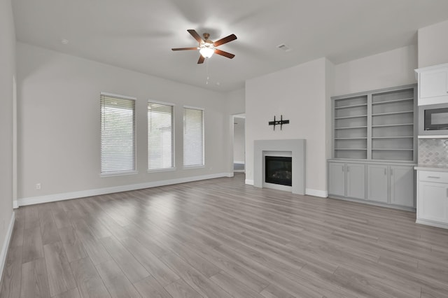 10066 Preserve Way, Conroe, TX 77385 - unfurnished living room featuring a glass covered fireplace, a ceiling fan, light wood-style flooring, and baseboards