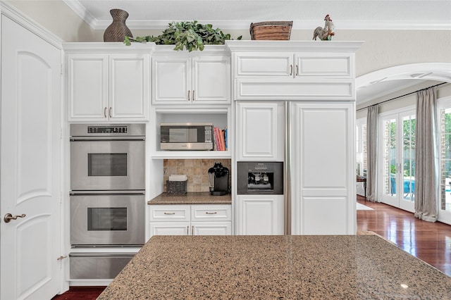 kitchen featuring stainless steel appliances, a warming drawer, arched walkways, ornamental molding, and light stone countertops