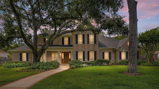 colonial home with a front lawn, brick siding, and a shingled roof