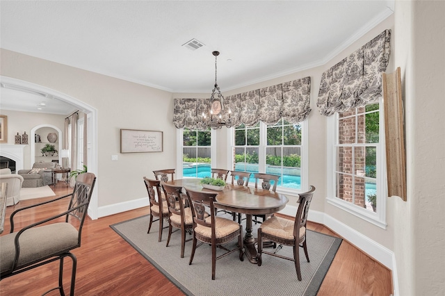 dining room with a fireplace, baseboards, wood finished floors, crown molding, and plenty of natural light