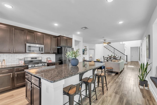 12311 Summerbrook Dr, Houston, TX 77066 - kitchen with appliances with stainless steel finishes, a breakfast bar area, a center island, dark brown cabinetry, and dark stone countertops