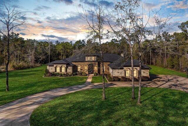 11410 Sunset Ave, Magnolia, TX 77354 - french country style house with curved driveway, a front lawn, stucco siding, and a forest view