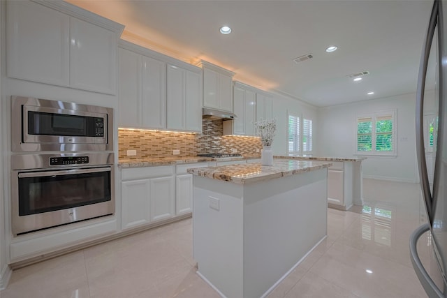 5411 Oban Terrace Ln, Sugar Land, TX 77479 - kitchen with stainless steel appliances, a kitchen island, under cabinet range hood, light tile patterned flooring, and decorative backsplash