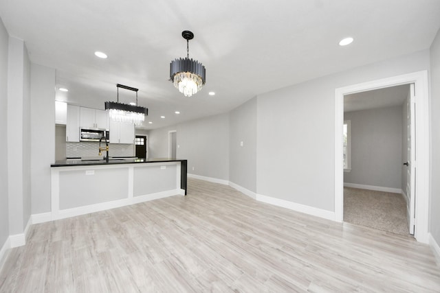 7622 Parker Rd, Houston, TX 77016 - kitchen with stainless steel microwave, dark countertops, a chandelier, white cabinets, and light wood finished floors