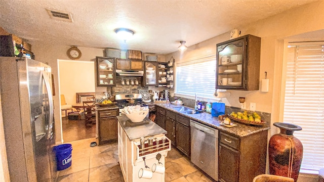 2822 Shotwell Ct, Missouri City, TX 77459 - kitchen featuring stainless steel appliances, under cabinet range hood, glass insert cabinets, a sink, and a textured ceiling
