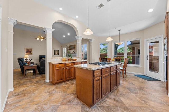5418 Brook Bend Dr, Sugar Land, TX 77479 - kitchen featuring ornate columns, stainless steel gas cooktop, brown cabinetry, a ceiling fan, and light stone countertops