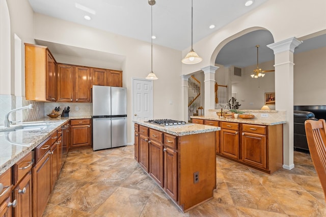 5418 Brook Bend Dr, Sugar Land, TX 77479 - kitchen with appliances with stainless steel finishes, decorative columns, a sink, brown cabinetry, and light stone counters
