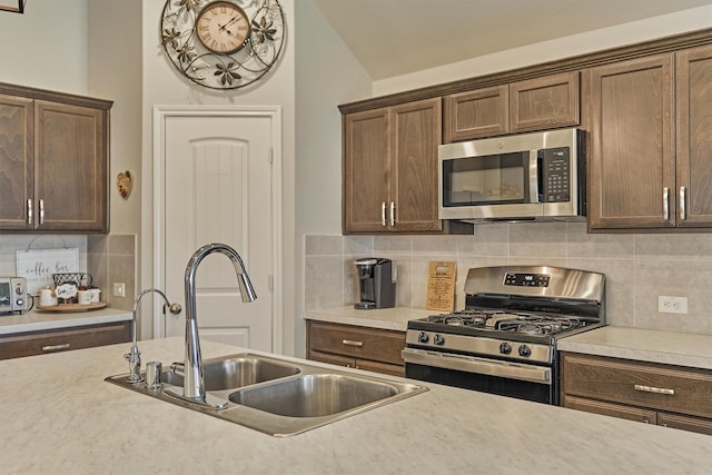 kitchen with appliances with stainless steel finishes, a sink, light countertops, decorative backsplash, and vaulted ceiling