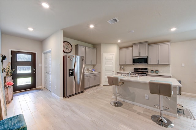12917 S Winding Pines Dr, Tomball, TX 77375 - kitchen featuring appliances with stainless steel finishes, gray cabinetry, a kitchen breakfast bar, backsplash, and a sink