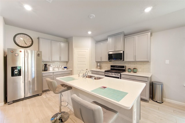 12917 S Winding Pines Dr, Tomball, TX 77375 - kitchen with stainless steel appliances, a sink, light wood finished floors, a center island with sink, and baseboards