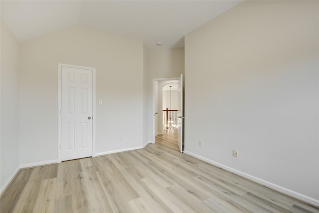 spare room with light wood-type flooring, baseboards, and vaulted ceiling