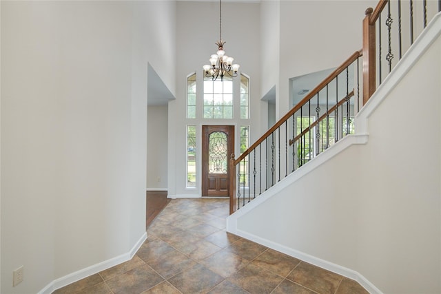 foyer entrance with baseboards, a chandelier, a towering ceiling, stairs, and stone finish floors