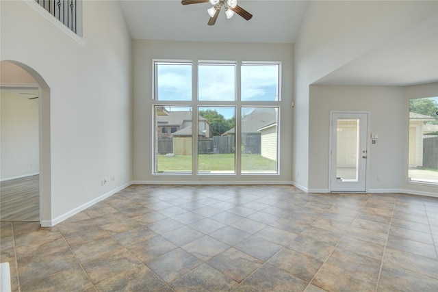 unfurnished living room featuring ceiling fan, baseboards, arched walkways, and high vaulted ceiling