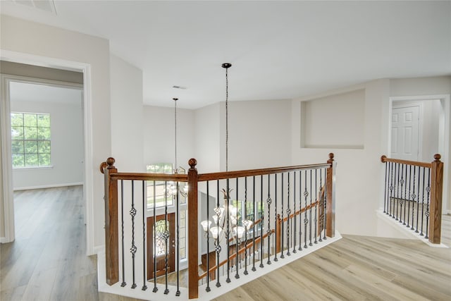 corridor featuring a chandelier, an upstairs landing, and wood finished floors
