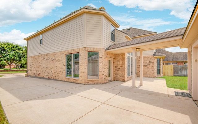 view of property exterior with brick siding, a patio area, fence, and roof with shingles