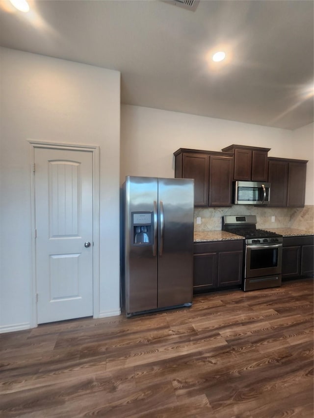 23716 Wood Green Terrace Dr, New Caney, TX 77357 - kitchen featuring appliances with stainless steel finishes, dark brown cabinets, tasteful backsplash, dark wood-type flooring, and light stone countertops