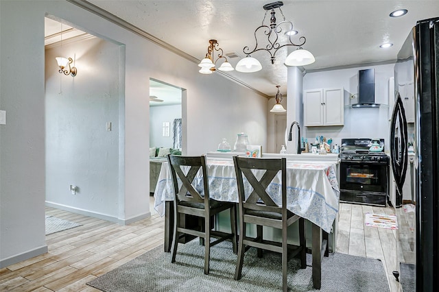873 W Santa Fe St, Conroe, TX 77301 - kitchen with black appliances, wall chimney exhaust hood, crown molding, light wood-type flooring, and white cabinets