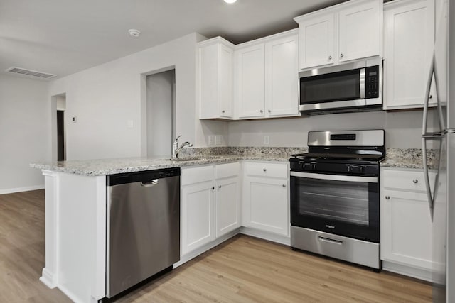15842 Berry Hill Dr, Conroe, TX 77303 - kitchen featuring appliances with stainless steel finishes, a peninsula, white cabinetry, and light wood-type flooring
