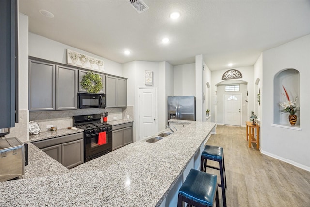 310 Morning Dove Trl, Sealy, TX 77474 - kitchen featuring black appliances, a sink, a kitchen bar, decorative backsplash, and light stone countertops