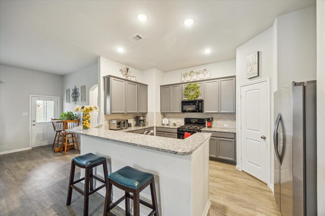 310 Morning Dove Trl, Sealy, TX 77474 - kitchen with black appliances, a peninsula, gray cabinetry, light wood-style floors, and tasteful backsplash