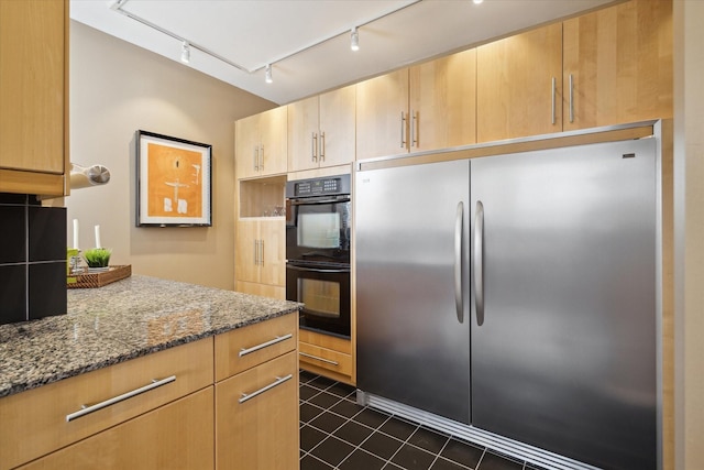 kitchen featuring stainless steel refrigerator, track lighting, dark stone countertops, light brown cabinetry, and dark tile patterned floors