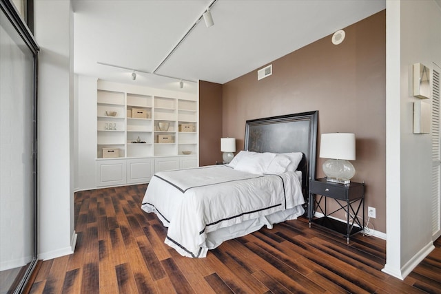 bedroom featuring track lighting, dark wood-style flooring, and baseboards