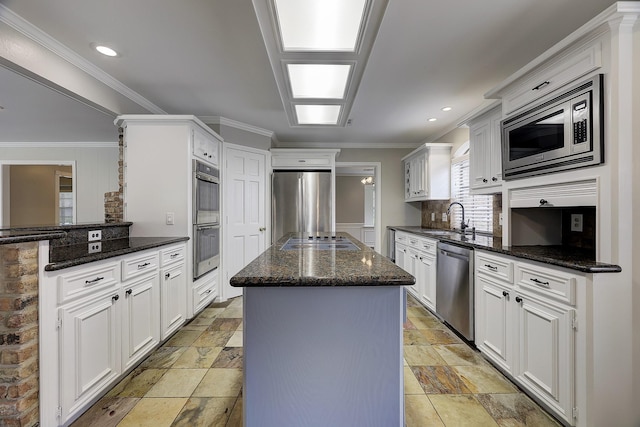 kitchen with stainless steel appliances, a sink, a kitchen island, dark stone countertops, and stone tile floors