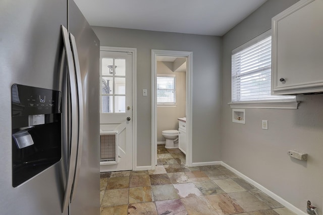 clothes washing area with stone tile flooring, baseboards, washer hookup, and cabinet space