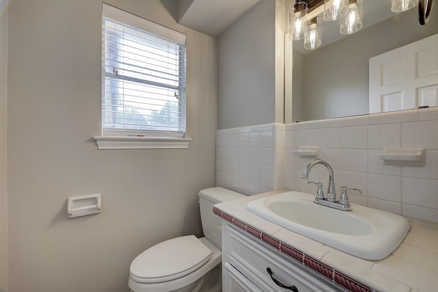 bathroom with toilet, plenty of natural light, vanity, and tile walls