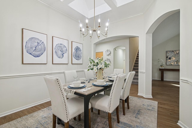 dining area featuring wood finished floors, baseboards, arched walkways, crown molding, and stairs