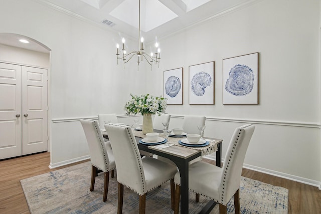 dining area featuring arched walkways, baseboards, wood finished floors, a chandelier, and ornamental molding