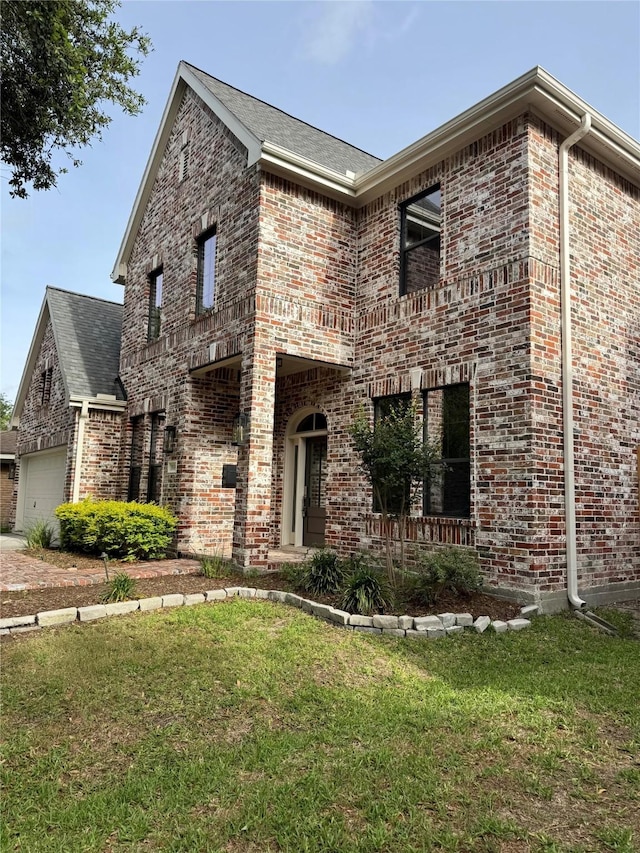 view of front of property featuring brick siding, a balcony, a garage, a front yard, and roof with shingles