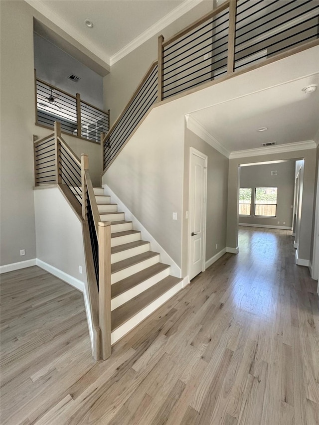 stairway with ornamental molding, wood finished floors, and baseboards