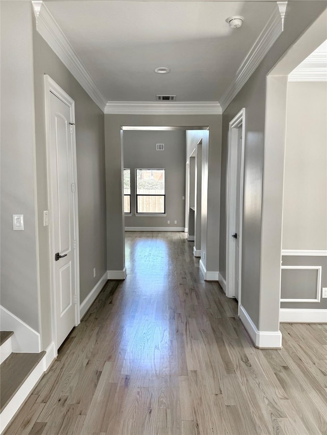 hall featuring crown molding, light wood-style flooring, baseboards, and stairway