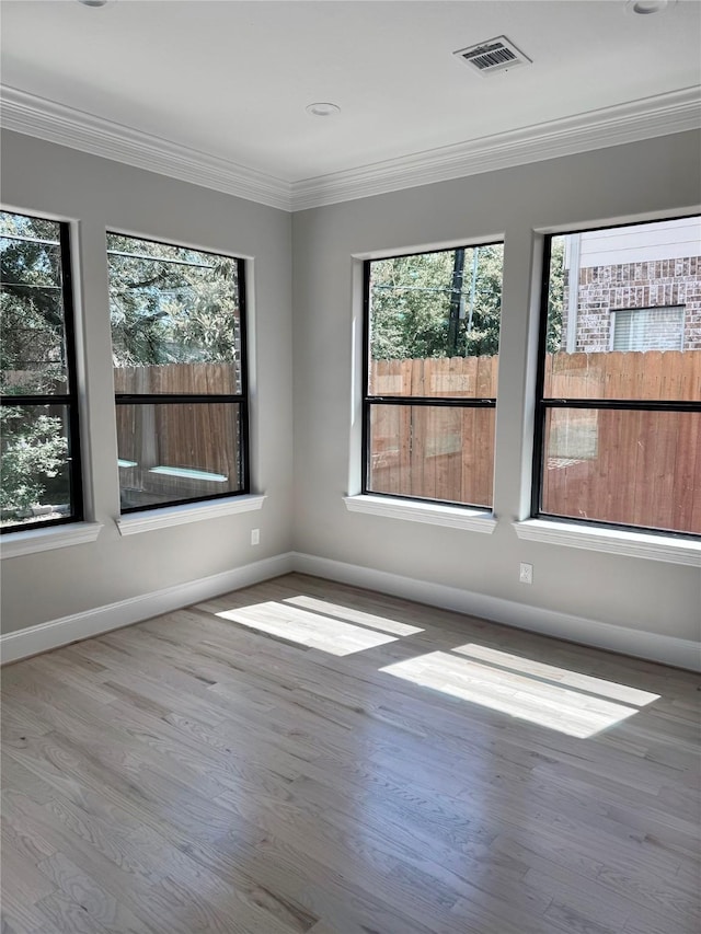 empty room featuring healthy amount of natural light, baseboards, wood finished floors, and ornamental molding