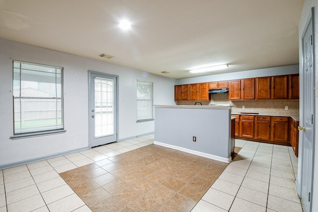15522 Noble Brook Ct, Houston, TX 77049 - kitchen with light tile patterned flooring, under cabinet range hood, brown cabinets, and tasteful backsplash
