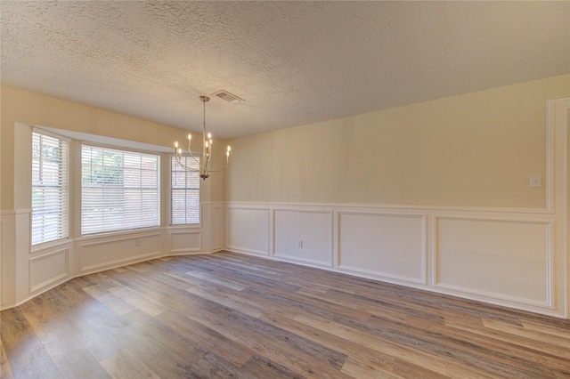unfurnished dining area with a decorative wall, a chandelier, wood finished floors, a wainscoted wall, and a textured ceiling